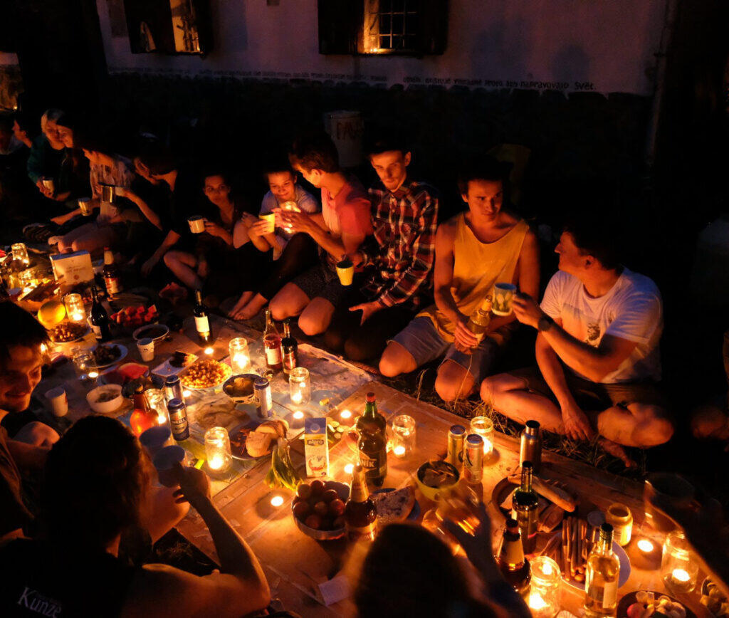 Dramatic, moody lighting over a chaotic banquet table where a human body is draped amongst a spread of raw food and fruits.
